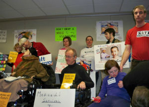 Individuals with disabilities speaking out against Medicaid cuts at public forum.